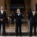 Three people in suits stand side by side in a marble lobby.