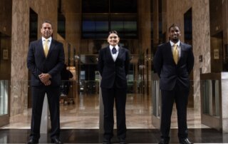 Three people in suits stand side by side in a marble lobby.