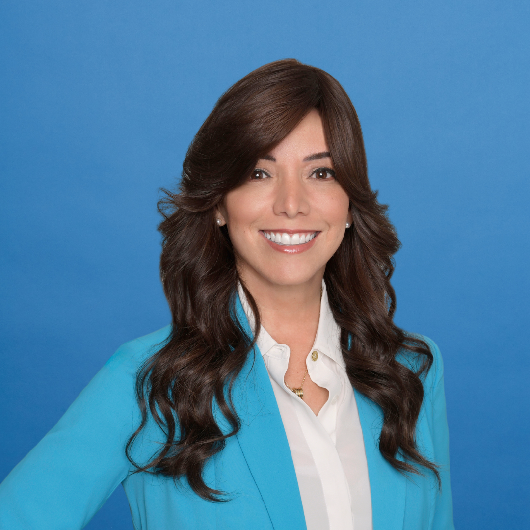 Woman with long brown hair in a blue blazer and white shirt smiling against a blue background.